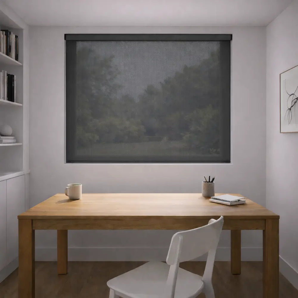 Charcoal Sunscreen Roller Shade fully closed in a home office, blocking glare on the desk while maintaining a clear view of the outdoors through the mesh fabric.