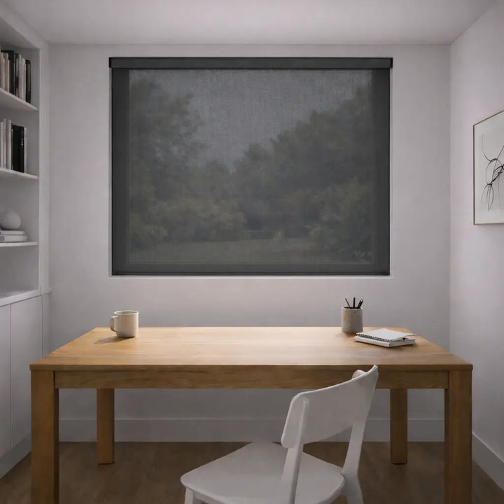 Charcoal Sunscreen Roller Shade fully closed in a home office, blocking glare on the desk while maintaining a clear view of the outdoors through the mesh fabric.